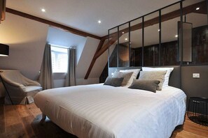 Een slaapkamer met een groot bed, een stoel en een raam met gordijnen.