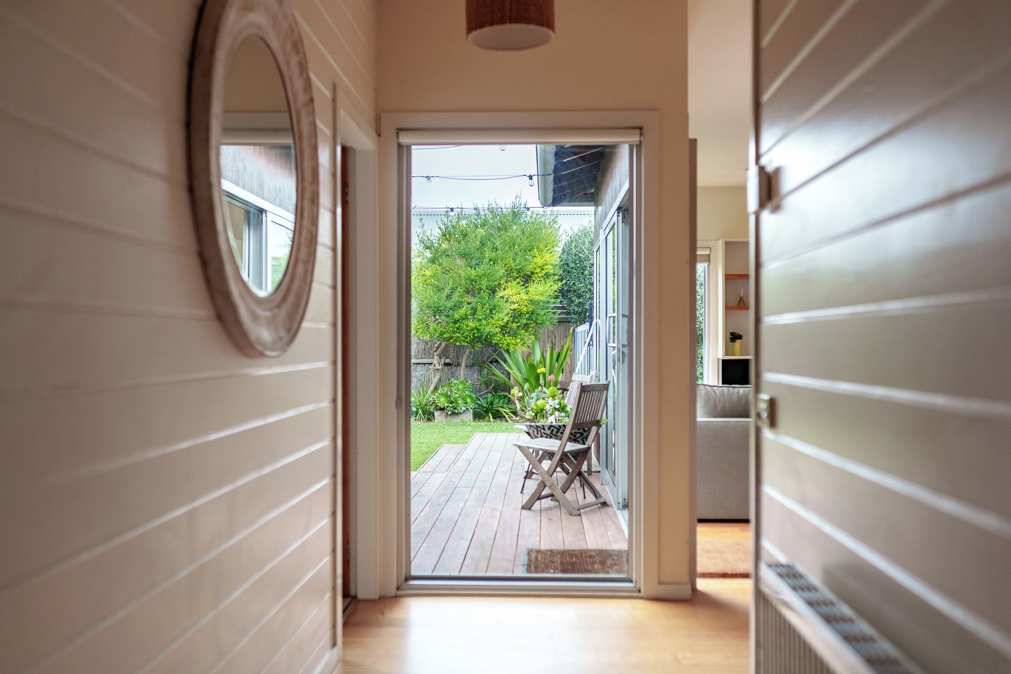 Un pasillo que da a un patio con terraza de madera y mobiliario exterior.