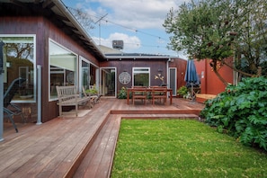 A wooden deck with a glass door leading to a patio area, a wooden bench, and a table with chairs.