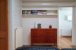 A room with a wooden dresser, a bookshelf with books, a vase, and a radiator.
