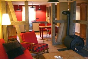 A cozy room with a red sofa, a plaid chair, a wooden table, and a black stove. - Holiday home in Tangermünde with Wi-Fi (Tangermünde)