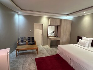 Ein Hotelzimmer mit einem Bett, einem Schreibtisch mit Spiegel, zwei Stühlen, einem roten Teppich und einem Kleiderschrank.