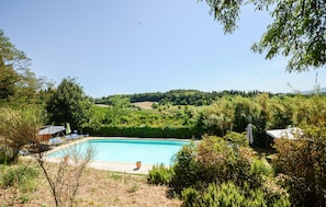 Ein Schwimmbecken, umgeben von Grün und Hügeln im Hintergrund.