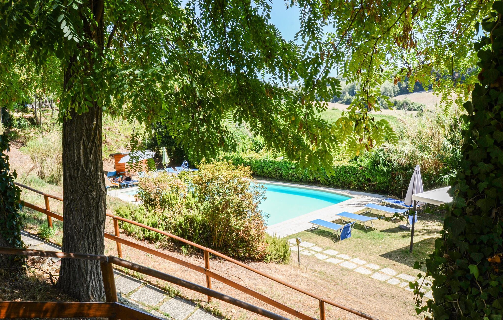 A pool area with lounge chairs and a small building, surrounded by trees and greenery.