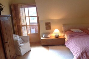 Een slaapkamer met een bed, nachtkastje, lamp en een stoel.