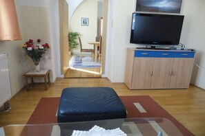 Een woonkamer met een televisie, een bank, een kast en een eethoek met stoelen en een tafel.