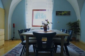 Een eetkamer met een gedekte tafel voor zes personen, een potplant op de tafel, en een raam met uitzicht op groen.