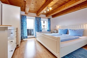Ein Schlafzimmer mit Holzboden, einem Bett mit blauer Bettwäsche, einem Schminktisch und einem Fenster mit blauen Vorhängen.