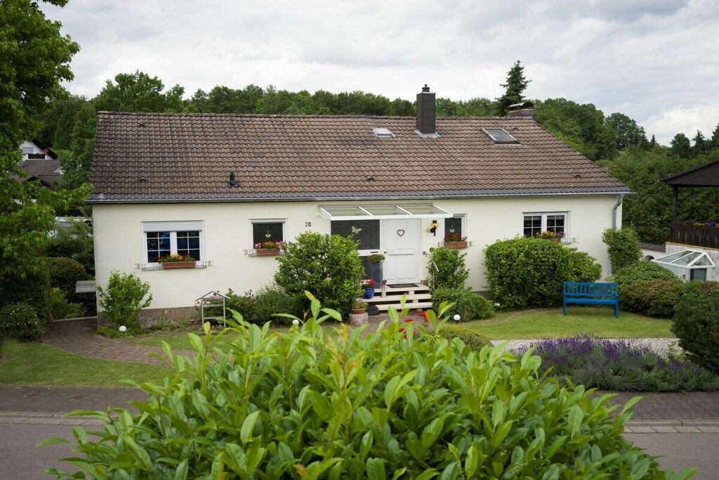 A two-story house with a tiled roof, a front porch, and a garden with a bench.