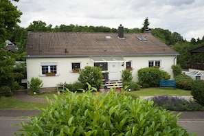A two-story house with a tiled roof, a front porch, and a garden with a bench. - Holiday apartment with 2 bedrooms (St. Wendel)