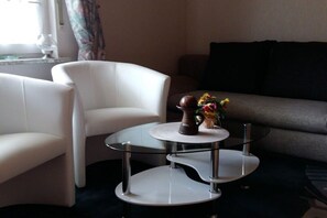 A modern living room with a glass coffee table, white armchairs, and a grey sofa. - Holiday apartment with 2 bedrooms (St. Wendel)