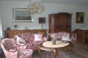 Een woonkamer met een bloemenbank, een ronde salontafel en een kroonluchter.
