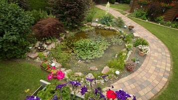 Un jardin avec un bassin, un chemin sinueux en briques et diverses plantes et fleurs.