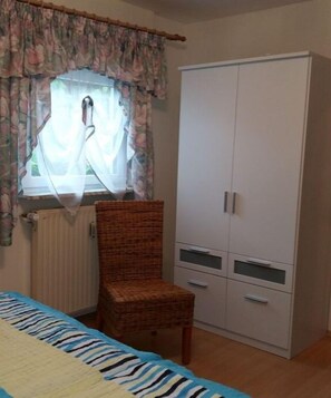 A bedroom with a bed, a chair, a wardrobe, and a window with curtains. - Holiday apartment with 2 bedrooms (St. Wendel)