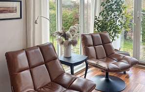 Two brown leather chairs with a modern design, a small table with a vase of dried plants, and a view of greenery through large windows. - Awesome home in Bjoa with WiFi (Bjoa)