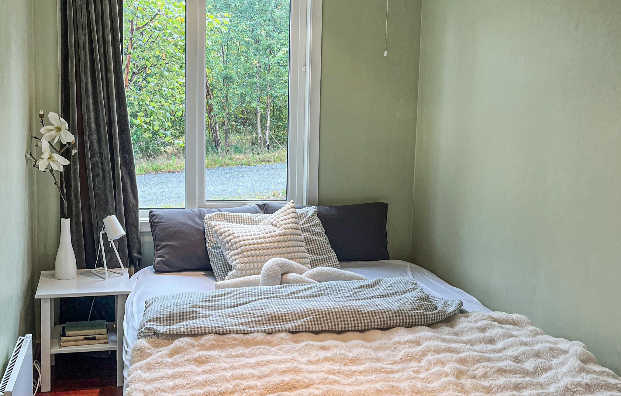 Une chambre à coucher avec un lit, une table de chevet avec une lampe, une fenêtre donnant sur un paysage verdoyant et un radiateur.