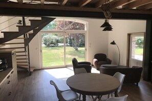 Ein modernes Interieur mit einer Treppe, einem Essbereich mit rundem Tisch und Stühlen sowie einer großen Schiebetür, die zu einem Garten führt.