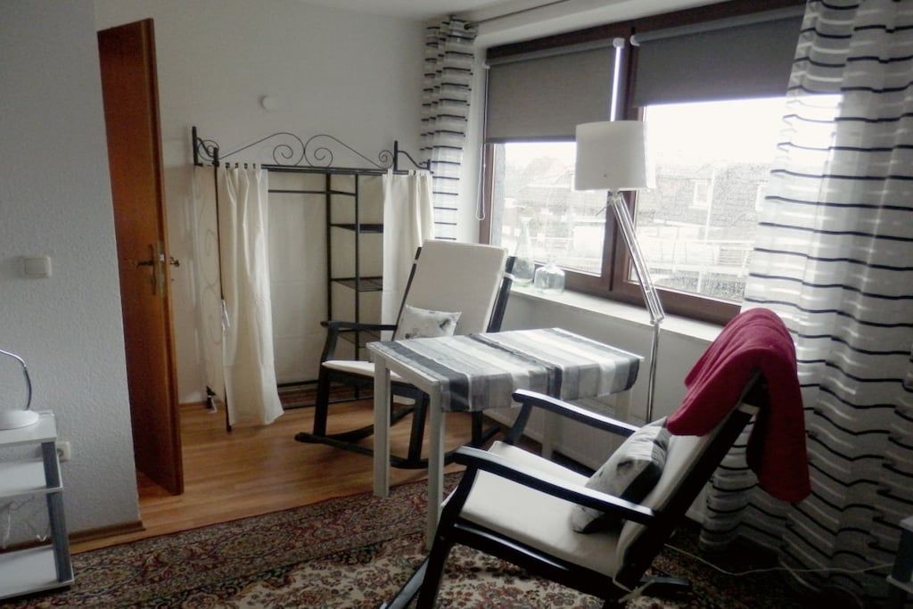 Een hotelkamer met een bed, een stoel, een tafel, een raam met gordijnen en een lamp.