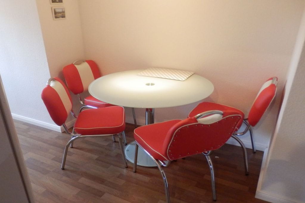 A dining area with a round table and six red chairs with white stripes.