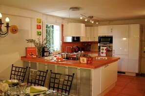 A kitchen with white cabinets, a central island, and a dining area with chairs and a table. - Holiday home in Gruissan with swimming pool (Gruissan)
