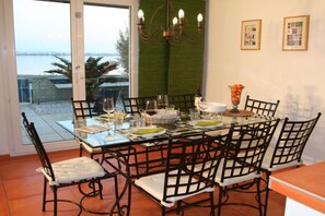 A dining area with a glass table, black chairs, and a view of the sea through a glass door. - Holiday home in Gruissan with swimming pool (Gruissan)
