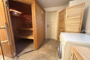 Ein Zimmer mit einer Holzauna, einer Waschmaschine und einer Tür zu einem weiteren Raum.