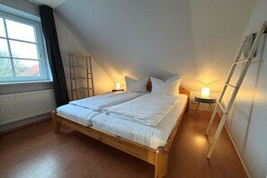 Ein Schlafzimmer mit einem Holzbett, einem Fenster mit Vorhängen, einer Hartsreppe und zwei Nachttischlampen.