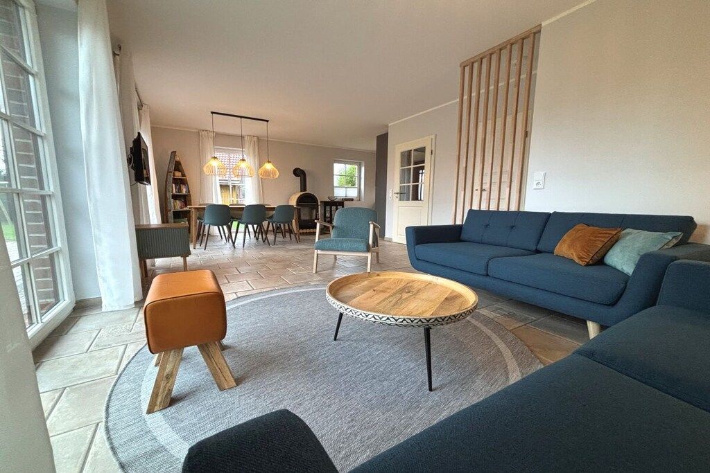 A living room with a blue sofa, a round coffee table, and a dining area with chairs and a table.