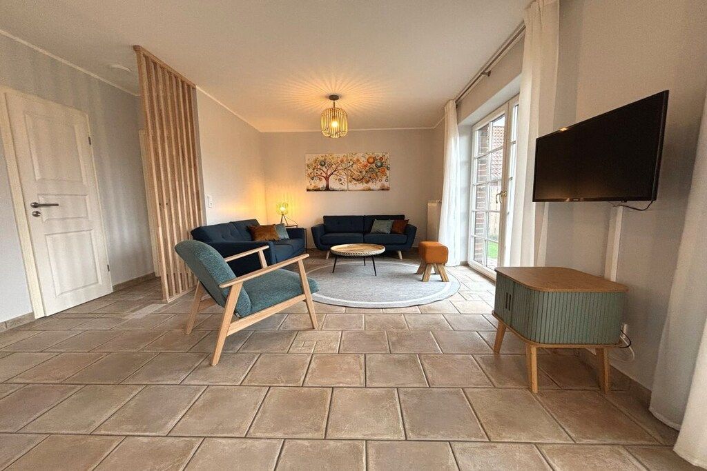 Een woonkamer met een bank, fauteuil, salontafel en een aan de muur bevestigde televisie.