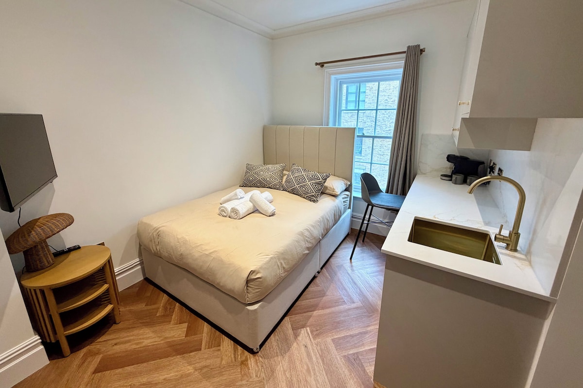 A hotel room with a bed, a TV, a desk with a chair, and a window with curtains.