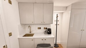 A compact kitchenette with a sink, coffee maker, and a chair. - Nestoya House (London)