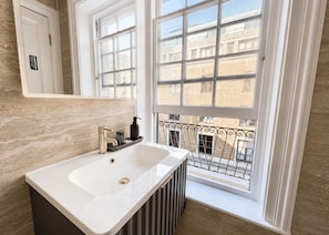 A bathroom with a white sink, a mirror, and a window with a view of buildings. - Nestoya House (London)