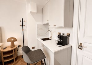 A compact kitchenette with a sink, a coffee maker, and a chair. - Nestoya House (London)