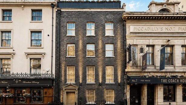 A row of three-story buildings with distinct architectural styles, including a black brick facade and a cream-colored building with a sign for 'Piccadilly's No.7 Private Club.' - Nestoya House (London)