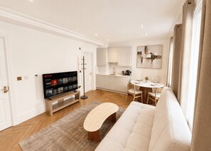 A modern living room with a flat-screen TV, a sofa, a coffee table, and a dining area with a table and chairs. - Nestoya House (London)
