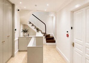 A hallway with a staircase, a white door, and a small plant on a cabinet. - Nestoya House (London)