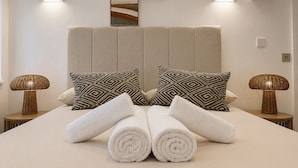 A neatly made bed with rolled towels, two patterned pillows, and two wall-mounted lamps. - Nestoya House (London)