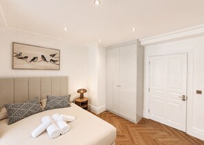 A bedroom with a bed, pillows, a nightstand, a lamp, a painting, and a wardrobe. - Nestoya House (London)