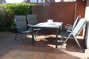 Une terrasse extérieure avec une table et des chaises, un mur en briques et une haie.