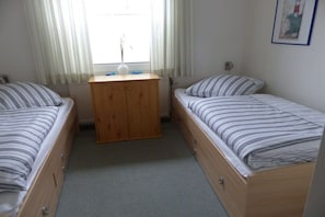 Ein Zimmer mit zwei Einzelbetten, einem hölzernen Nachttisch, einer Vase und einem gerahmten Bild an der Wand.