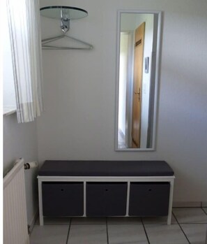 Ein Zimmer mit einer weißen Bank, einer hängenden Leuchte und einem Spiegel, der eine Tür widerspiegelt.