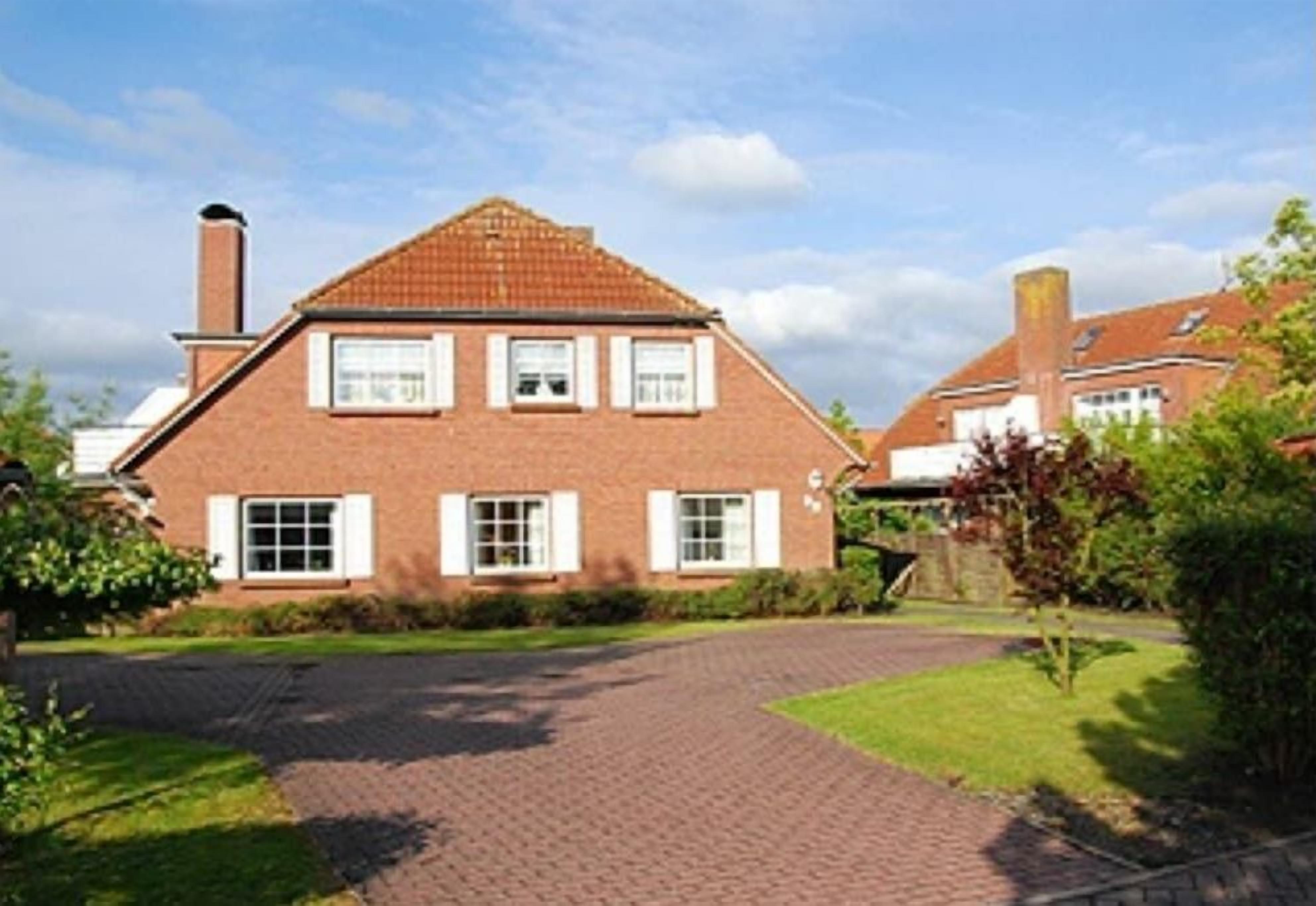 A two-story brick house with a tiled roof, a paved driveway, and a well-maintained lawn.
