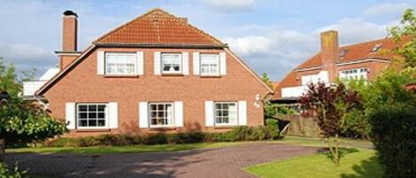 A two-story brick house with a tiled roof, a paved driveway, and a well-maintained lawn.