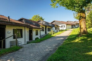 A row of white buildings with tiled roofs, a paved pathway, and a tree on the right. - Holiday home in Allgäu with 1 bedroom (Lechbruck)