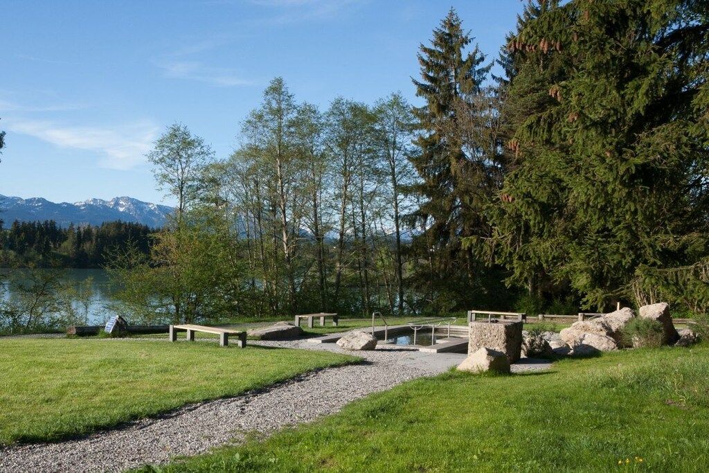 Ein Park am Seeufer mit einem Kiesweg, Bänken und einer kleinen Brücke über dem Wasser.