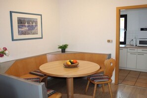 A dining area with a round table, wooden chairs, a fruit bowl, a framed picture, and a potted plant. - Holiday home in Allgäu with 1 bedroom (Lechbruck)