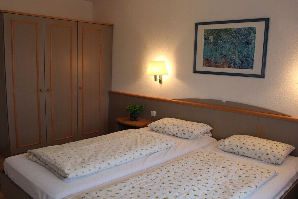 Une chambre d’hôtel avec un lit double, une table de chevet avec une lampe, une armoire et un tableau encadré au mur.
