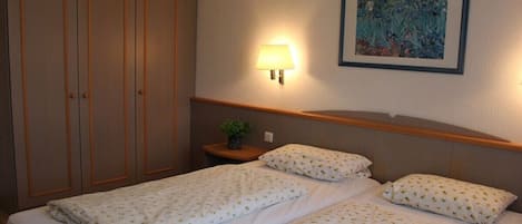 Een hotelkamer met een tweepersoonsbed, een nachtkastje met lamp, een kledingkast en een lijst aan de muur.