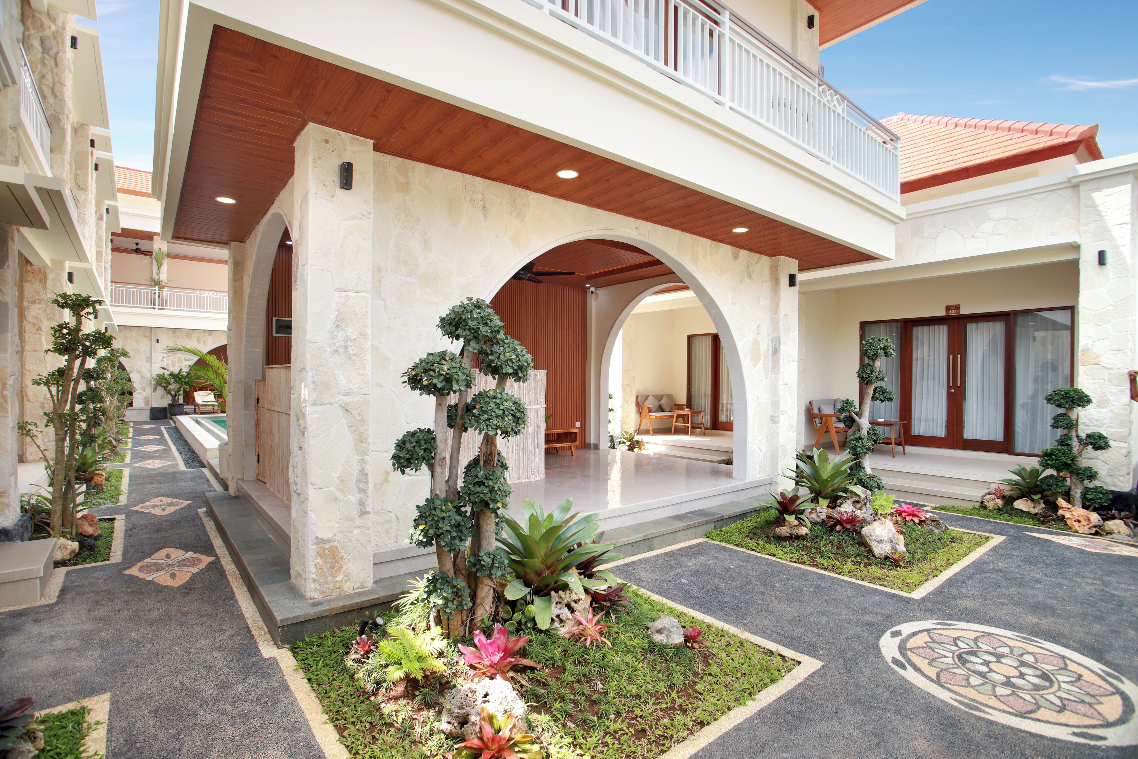 A modern building with a covered walkway, stone walls, and a variety of plants.
