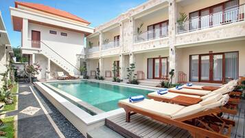 A hotel with a swimming pool, lounge chairs, and a staircase leading to the upper floors.